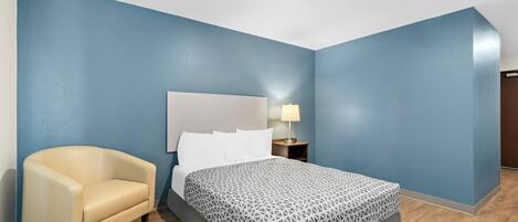 Une chambre d’hôtel avec un lit, une chaise, une table de chevet avec une lampe et des murs bleus.