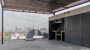 Una terraza en la azotea con zona de barbacoa, vistas del horizonte de la ciudad y un área de estar cubierta.