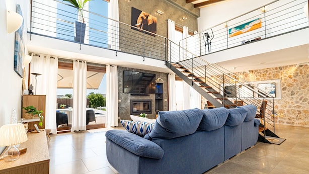 A spacious living area with a blue sofa, a staircase, and a stone wall. - VILLA NIMAF - SA PLANERA (Marratxi)