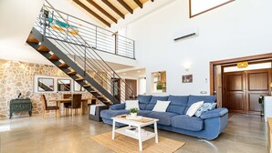 A spacious living room with a blue sofa, a dining table, and a staircase leading to an upper level. - VILLA NIMAF - SA PLANERA (Marratxi)