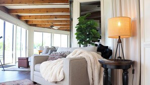 Ein gemütliches Wohnzimmer mit einer Couch, einer Lampe und einer großen Pflanze.
