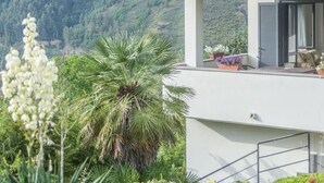 A modern house with a red-tiled roof, a balcony with potted plants, and a lush green landscape in the background. - Villa in Vigna Apartment (San Mango sul Calore)