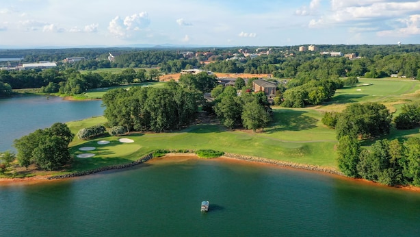 Ein Golfplatz mit einem See, umgeben von Bäumen und Gebäuden.