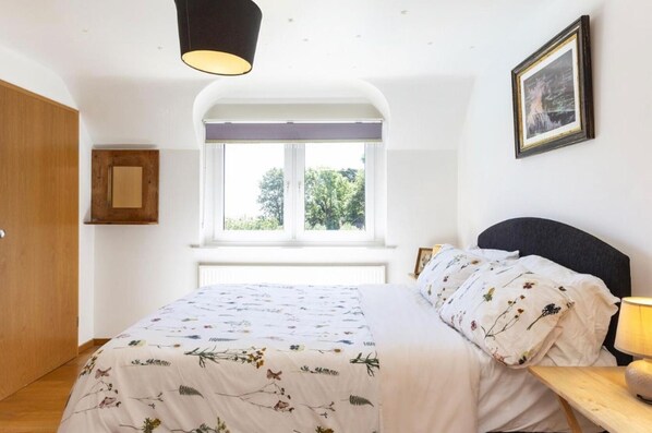 A bedroom with a bed, a window, a door, a bedside table, a lamp, and a framed picture on the wall. - Sleeps10/18-parking-garden-pool-hottub-balcony (Eastbourne)