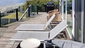 Une terrasse avec des chaises longues et une table, offrant une vue sur une plage et l’océan.