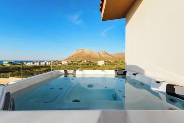 A hot tub with a clear view of a mountainous landscape and the sea in the background.