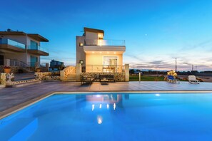 A modern two-story house with a swimming pool, outdoor seating, and a stone facade.