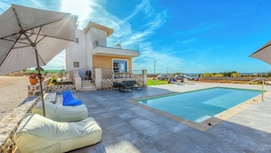 Una vila moderna amb piscina, mobiliari exterior i vista despejada al mar.
