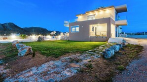 Una casa moderna de dos pisos amb teulada plana, grans finestres i interior ben il·luminat.