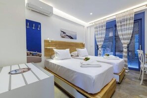 A modern hotel room with two beds, a wooden headboard, a blue accent wall, and a view through a window with patterned curtains.