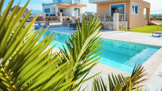 Zona de piscina moderna amb una piscina de blau clar, envoltada de palmeres i un edifici contemporani amb diversos pisos i balcons.