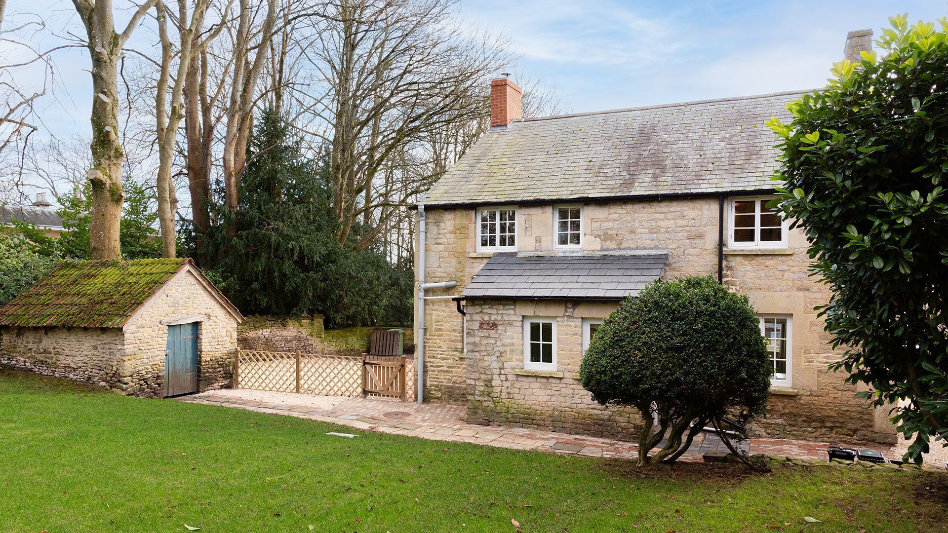 A stone house with a sloped roof, a small attached shed, and a well-maintained lawn.