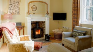 A cozy living room with a fireplace, comfortable seating, a television, and a patterned curtain.
