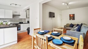 Een moderne keuken met witte kasten, een eettafel gedekt met blauwe borden, en een grijze bank in de woonkamer.
