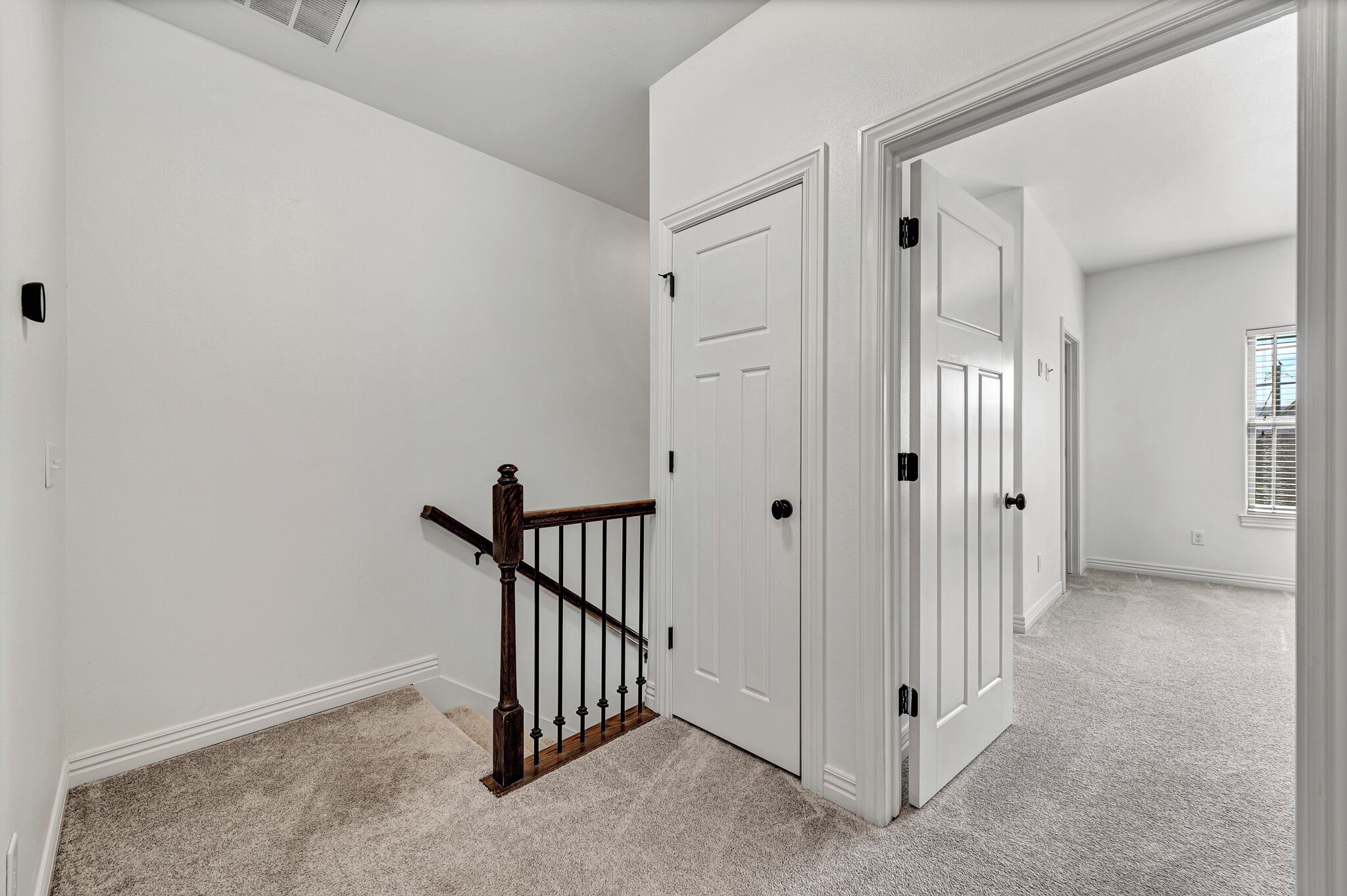 A hallway with white walls, a carpeted floor, and a wooden staircase with black balusters.