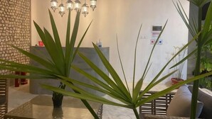 A dining area with a glass table, potted plants, hanging lights, and a stone wall.