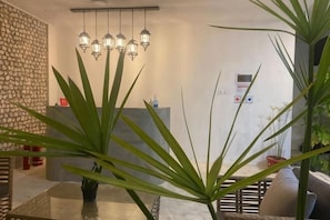 A dining area with a glass table, potted plants, hanging lights, and a stone wall.