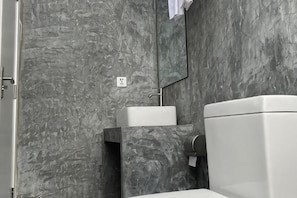 A bathroom with a marble wall, a white sink, and a toilet. - Coral Castle Guest House (Goidhoo)