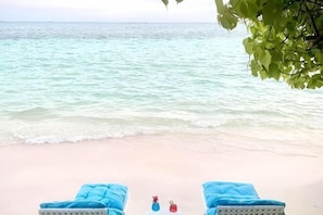 Blick auf einen Strand mit zwei Liegestühlen und einer Flasche im Sand.