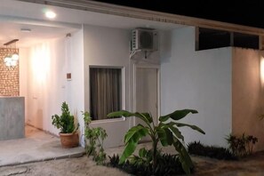 Exterior de un edificio residencial de noche, con una entrada bien iluminada, una puerta y una ventana.