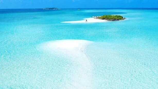 A clear turquoise sea with a small island and a sandy beach.