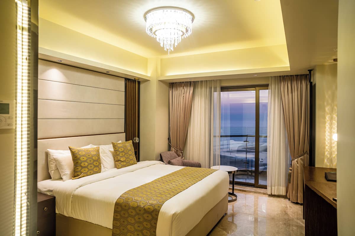 Une chambre d’hôtel avec un grand lit, un lustre, un balcon avec des rideaux et un bureau.