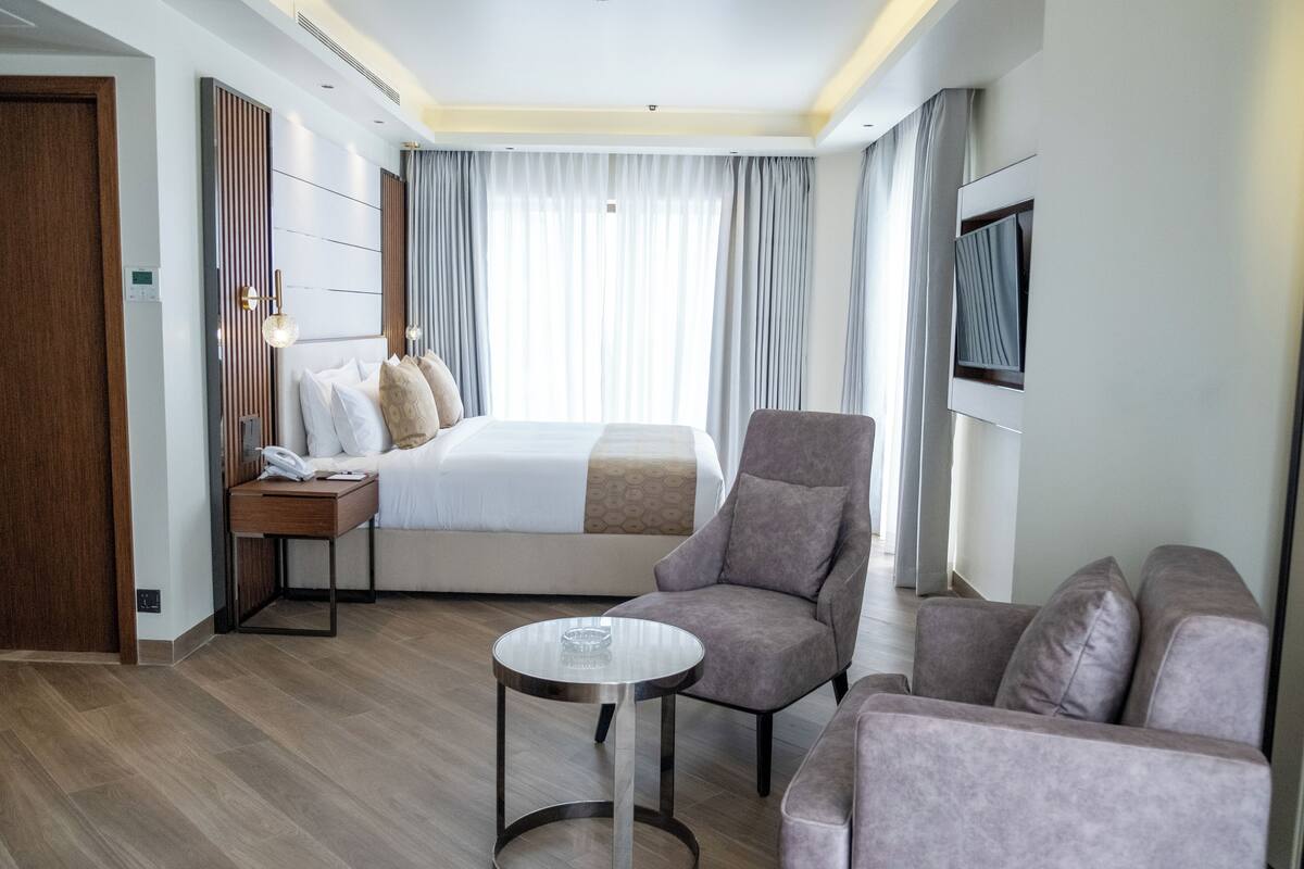 Une chambre d’hôtel moderne avec un lit bien fait, un canapé, une petite table et un téléviseur fixé au mur.