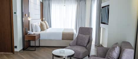 A modern hotel room with a neatly made bed, a sofa, a small table, and a TV mounted on the wall.