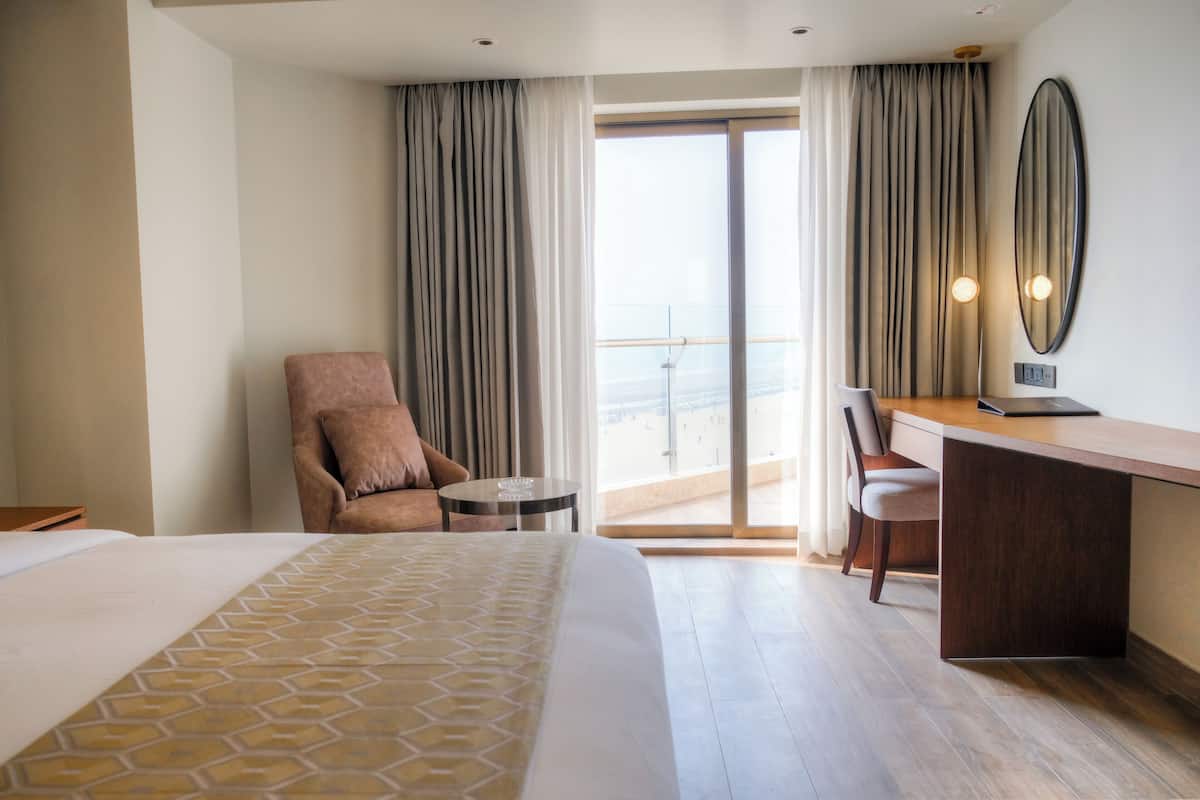 Une chambre d’hôtel avec un grand lit, un bureau, une chaise et une vue sur la ville depuis un balcon.
