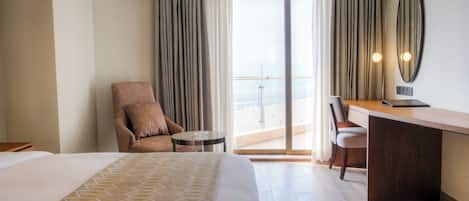 A hotel room with a large bed, a desk, a chair, and a view of the city through a balcony.