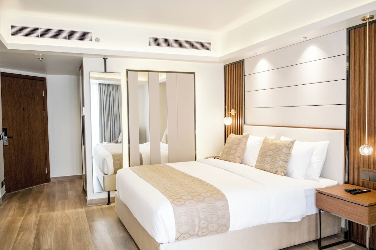 Une chambre d’hôtel moderne avec un grand lit, une table de chevet en bois et un miroir.