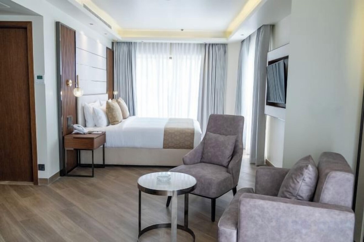 A hotel room with a bed, a sofa, a small table, and a TV on the wall.
