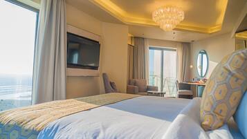 Habitación de hotel con una cama grande, un televisor montado en la pared, un escritorio con una silla y vista al océano.