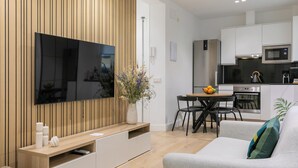 Una sala de estar moderna con televisor de pantalla plana, una pared de acento de madera, un comedor con mesa y sillas, y una cocina con electrodomésticos de acero inoxidable.