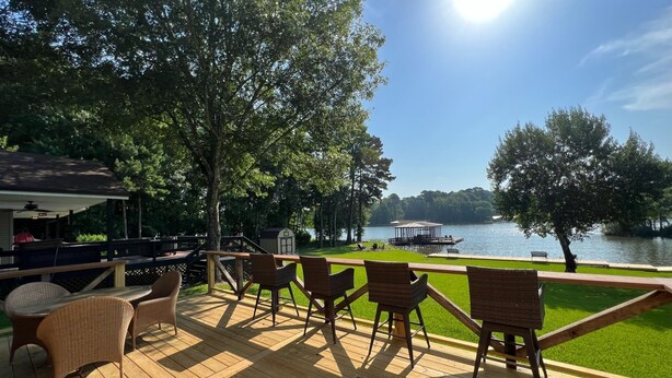 Eine Holzterrasse mit Korbstühlen mit Blick auf einen See, einem Pavillon und einem überdachten Grillbereich.
