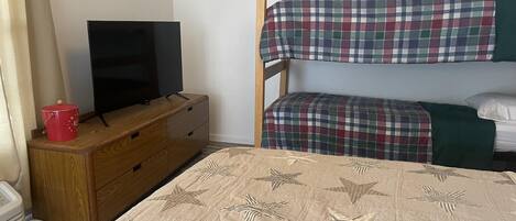 A bunk bed with plaid bedding, a wooden dresser with a television, and a star-patterned bedspread.