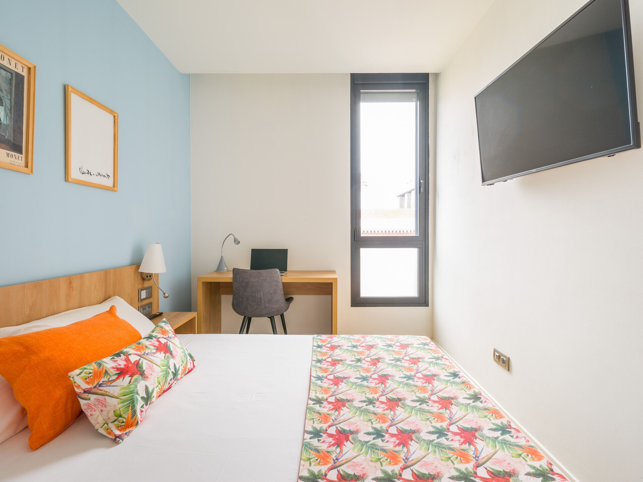 Hotellihuone, jossa on sänky, työpöytä, tuoli, televisio ja ikkuna.