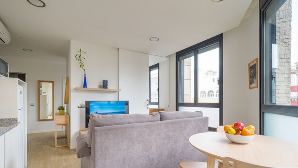 A modern kitchen with a built-in oven, a dining area with a grey sofa and a round wooden table, and a large window with a city view. - VIVENTE 3A BY CANARIAS GETAWAY (Las Palmas de Gran Canaria)