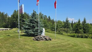 Une zone herbeuse avec trois drapeaux, un panneau indiquant le « White Fatig Motel » et une statue sur un rocher.