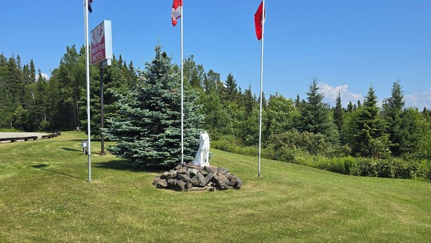 A grassy area with three flags, a sign for the White Fatig Motel, and a statue on a rock. - White Fang Motel (Wawa)