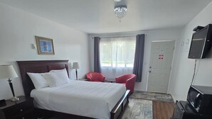 A hotel room with a large bed, a desk with a chair, a TV, and a window with curtains. - White Fang Motel (Wawa)