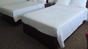 Une chambre d’hôtel avec deux lits simples, une table de chevet avec une lampe et un tableau encadré au mur.