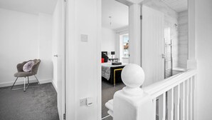 Un couloir moderne et minimaliste, avec un tapis gris, une porte blanche donnant sur une chambre et une rambarde blanche surmontée d’un élément décoratif sphérique.