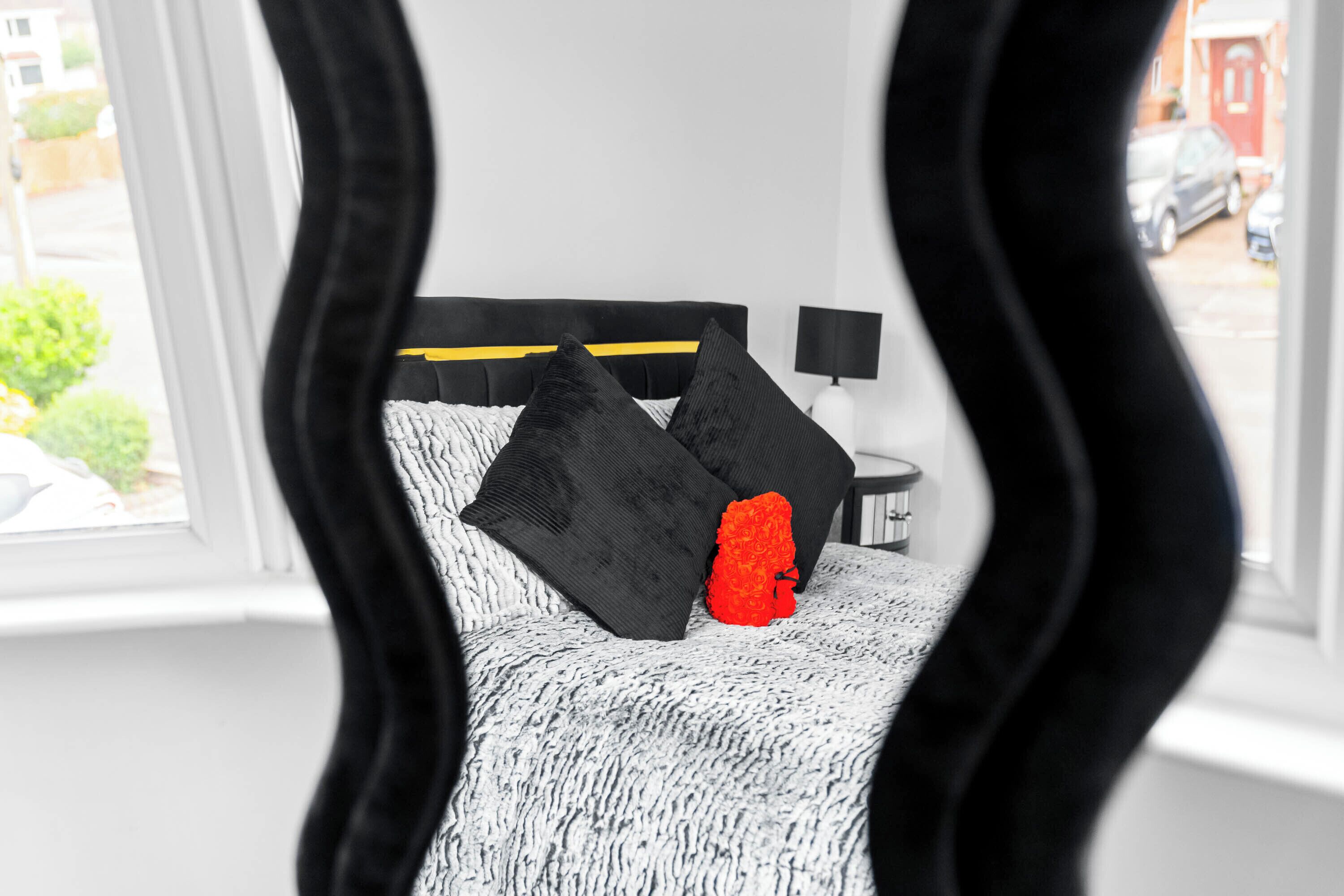 A bedroom with a bed, black and white bedding, a red pillow, and a nightstand with a lamp.