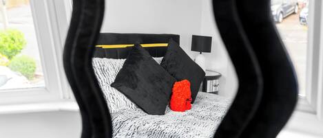 A bedroom with a bed, black and white bedding, a red pillow, and a nightstand with a lamp.