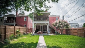 Ein zweistöckiges Haus mit einer Veranda, einem Holzzaun und einem kleinen Garten mit einem Baum und einer Hängematte.