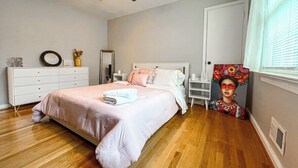 Ein Schlafzimmer mit einem Bett, einem Schminktisch, einem Deckenventilator, einem Fenster mit Jalousien und einem Bild an der Wand.