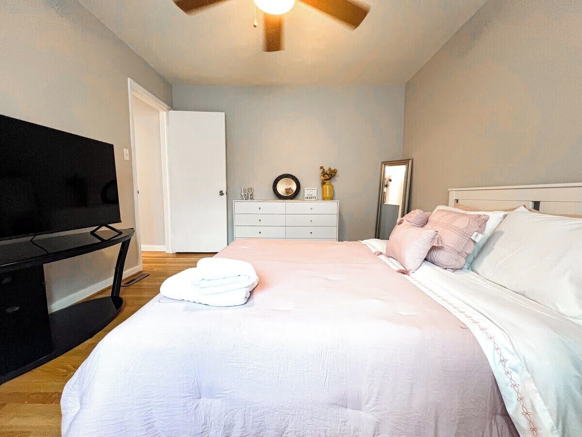 A bedroom with a bed, a TV, a dresser, and a mirror.
