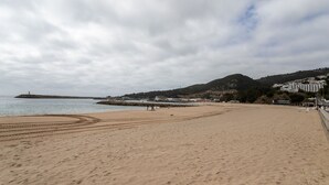 A wide sandy beach with a rocky breakwater in the distance, a few people, and buildings on a hillside. - Sesimbra Beach Apartment by GT House (Sesimbra)