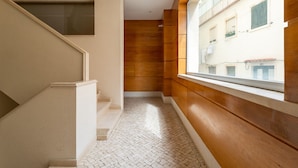 A narrow hallway with a tiled floor, a wooden wall, and a window overlooking a building with balconies. - Sesimbra Beach Apartment by GT House (Sesimbra)